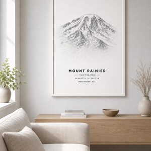 May include: A framed wall art print featuring a detailed black and white line drawing of Mount Rainier. The text reads MOUNT RAINIER, 14,436 ft (4,392 m), 46.8523° N, 121.7603° W, and WASHINGTON, USA, centered below the mountain illustration.
