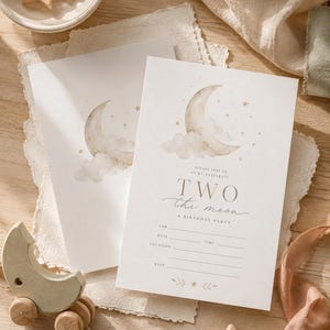 Könnte beinhalten: Zwei Geburtstagseinladungen mit einem Aquarell-Mond und Sternen-Design. Der Text lautet "Two the moon" mit Ausfüllfeldern für Datum, Uhrzeit und Ort. Holzspielzeug in Form von Sternen und Monden sind ebenfalls im Bild.