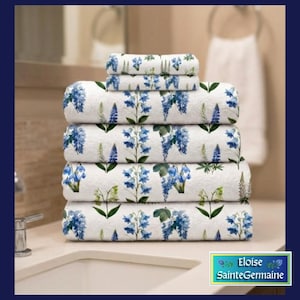 May include: A stack of five white towels featuring a repeating botanical print of blue bell-shaped flowers and green leaves. The towels are folded neatly in a pile, displaying a consistent floral pattern across each piece of the set.
