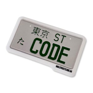 May include: A rectangular sticker designed to look like a license plate. It has the words "TOKYO ST CODE" in green on a grey background, with a white border. The website address www.streetcode.uk is also visible.