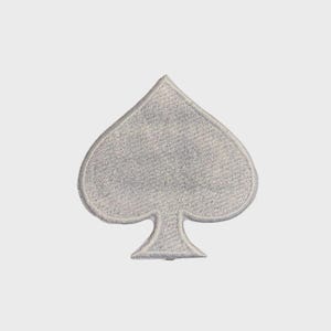May include: A silver-colored embroidered patch in the shape of a spade playing card suit symbol. The patch has a textured appearance and a white border, set against a plain white background.