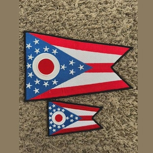 May include: Two Ohio state flag patches. The patches feature a blue triangle with white stars and a red circle, and red and white stripes. The patches are in different sizes.