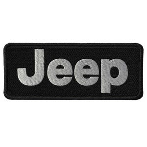 May include: Black rectangular patch with the word "Jeep" embroidered in silver thread. The patch has a textured surface and rounded corners. The Jeep logo is a popular emblem for automotive enthusiasts.