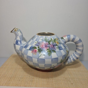 May include: A ceramic teapot featuring a light blue and white checkered pattern across the body and a blue and white striped handle. The surface is decorated with a floral arrangement of pink roses and purple flowers. It has a gold-trimmed rim.
