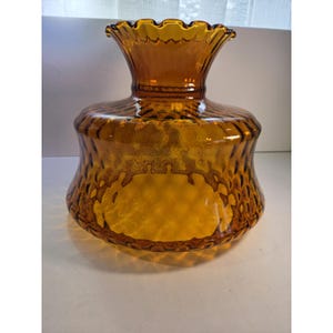May include: Amber-colored glass lamp shade with a ruffled top and textured body. The shade has a wide, rounded base and a narrower, flared top. The glass has a mottled appearance, with darker brown accents throughout. The shade is designed to diffuse light.