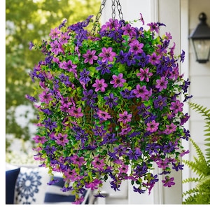 May include: A hanging basket filled with artificial flowers in shades of purple and violet, featuring small five-petaled blossoms and green foliage. The arrangement is suspended by a black metal chain, creating a dense, rounded floral display.