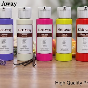 Puede incluir: Cinco botellas coloridas de aceite perfumado "Kick Away" con aromas como Lavanda, Vainilla, Pink Sugar, Melocotón y Mantequilla de Mango. Las botellas están dispuestas sobre una superficie de madera con frutas y flores.