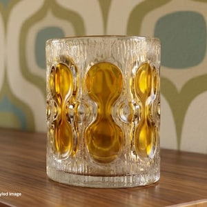 May include: A cylindrical glass candle holder featuring a textured, bark-like exterior surface and a repeating pattern of smooth, amber-colored circular indentations arranged vertically around the entire circumference of the clear glass vessel.