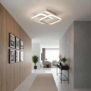 May include: Contemporary white ceiling light with a geometric design, in a hallway. The light has a square base with two overlapping square rings. The hallway features wood panelling, framed black and white photos, and a neutral-toned rug.