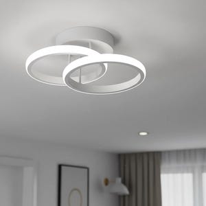 May include: A modern white ceiling light fixture featuring two overlapping circular light rings. The rings are illuminated with bright white light, creating a contemporary design. The fixture is mounted on a white ceiling.
