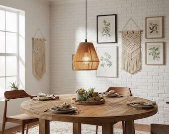 May include: A pendant light with a woven, conical shade hangs above a wooden dining table. The light fixture is suspended from a black ceiling mount. The dining room features a white brick wall, framed botanical prints, and macrame wall hangings.