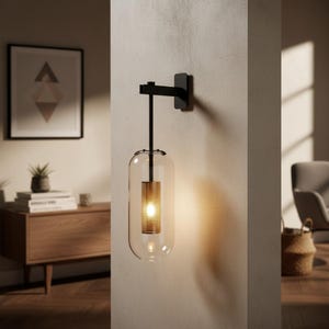 May include: A modern wall sconce with a black metal arm and a clear glass shade. The shade has a cylindrical, textured, gold-colored interior that houses a warm light. The sconce is mounted on a neutral-colored wall, creating a minimalist aesthetic.