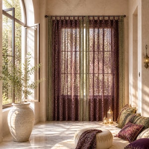 Puede incluir: Un interior soleado con cortinas estampadas en tonos burdeos y verde oliva. Un jarrón grande con una planta cerca de una ventana abierta. Un otomán redondo con una manta con flecos y cojines decorativos.