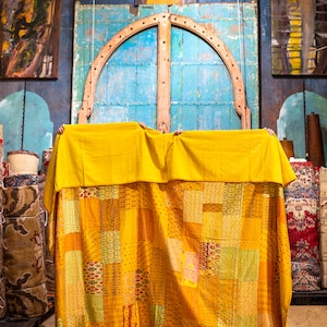 May include: A yellow patchwork quilt with a variety of patterns and textures. The quilt is hanging from a door frame and is partially covering a doorway.