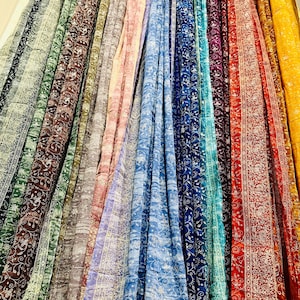May include: A display of flowing fabric in various colors, including green, brown, blue, and red. Each fabric panel features a detailed, repeating floral pattern in white. The fabrics are likely intended for clothing or home decor.