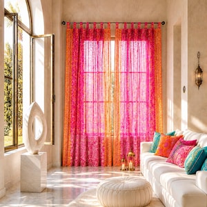 Puede incluir: Un salón luminoso con cortinas estampadas en rosa y naranja vibrantes que enmarcan una ventana. Un sofá blanco está adornado con cojines coloridos. Un otomán blanco descansa sobre una alfombra mullida y una escultura de mármol añade un toque artístico.
