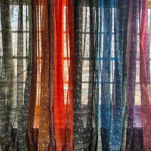 Pode incluir: Um conjunto de cortinas transparentes em várias cores, incluindo preto, marrom, laranja, azul e roxo. As cortinas têm um padrão floral e estão penduradas na frente de uma janela.