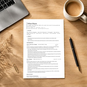 Può includere: Un curriculum vitae intitolato "Ethan Hayes" è esposto su una scrivania di legno, insieme a un laptop, una tazza di caffè, una penna e una graffetta. Il curriculum vitae descrive l'esperienza professionale e l'istruzione.