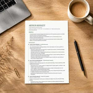 Può includere: Un curriculum vitae intitolato "ARTHUR BENNETT" è su una scrivania di legno, accanto a un laptop, una tazza di caffè, una penna e una graffetta. Il documento elenca l'esperienza e le competenze professionali. Il testo è in nero.