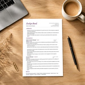 Può includere: Un curriculum vitae intitolato "Evelyn Reed, Senior Account Strategist" è su una scrivania di legno, accanto a un laptop, una tazza di caffè, una penna e una graffetta. Il curriculum elenca l'esperienza e le competenze nella gestione degli account e nella pianificazione strategica.