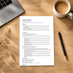 Può includere: Un curriculum vitae intitolato "Sarah Jenkins" è su una scrivania di legno, con un laptop, una tazza di caffè, una penna e una graffetta. Il curriculum elenca l'esperienza professionale e le competenze.