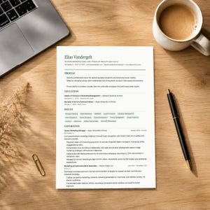 Può includere: Un curriculum vitae intitolato "Elias Vandergelt" è esposto su una scrivania di legno, insieme a un laptop, una tazza di caffè, una penna e una graffetta. Il curriculum include sezioni per profilo, istruzione, competenze ed esperienza.