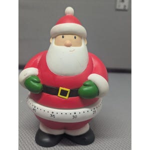 May include: A Santa Claus kitchen timer featuring a red suit with white trim, green mittens, and black boots. The midsection of the figure includes a white band with black numerical markings ranging from 25 to 40, used for tracking time intervals.