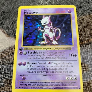 May include: A holographic Mewtwo trading card with a purple border, featuring the character in the center, the text Psychic and Barrier, and the 1st Edition stamp. The card displays 60 HP, genetic information, and the year 1999 at the bottom.