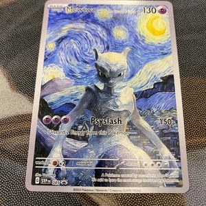 Peut inclure: Une carte à collectionner Mewtwo avec un style artistique inspiré de La Nuit étoilée, incluant un croissant de lune jaune et un ciel bleu tourbillonnant. La carte affiche 130 PV, l'attaque Psyslash et le numéro de série 085.