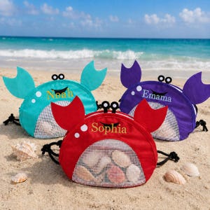 May include: Three crab-shaped drawstring bags in teal, purple, and red, each featuring a mesh front panel, two raised eyes, and two claws. The bags are personalised with the embroidered names Noah, Emama, and Sophia, and contain various seashells.