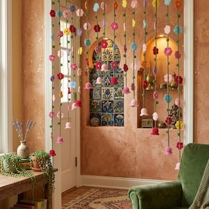 May include: A decorative door curtain featuring multiple vertical strands of green yarn suspended from a horizontal rod. Each strand is adorned with small, multi-colored crocheted flowers and bell-shaped blossoms in shades of pink, red, blue, and yellow.