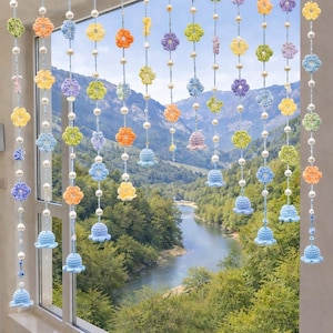 Peut inclure: Une suspension décorative pour fenêtre composée de multiples brins verticaux en fil bleu clair. Chaque brin est orné de petites fleurs crochetées multicolores dans des tons jaune, orange, vert et violet, entremêlées de perles blanches et de clochettes bleu clair.