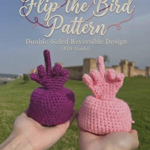 Peut inclure: Deux figurines crochetées, une violette et une rose clair, chacune en forme de main faisant un geste de doigt d'honneur. Le texte Flip the Bird Pattern Double-Sided Reversible Design (PDF Guide) est affiché au-dessus des deux objets.