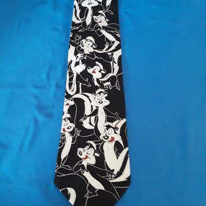 Peut inclure: Une cravate noire avec un motif répété de moufettes de dessin animé en blanc et noir. Les moufettes ont des accents rouges. La cravate est en tissu lisse. Le fond est bleu.