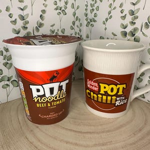 May include: A white and red Pot Noodle cup with "Beef & Tomato" flavor and a white mug with "Golden Wonder Chili Pot with Rice" printed on it. The cup says "Get Charged Up in 4 Minutes".