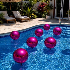 May include: Seven spherical pool floats with a smooth, reflective magenta finish are distributed across the surface of a blue swimming pool. Each orb features a glossy, metallic texture that catches the sunlight, creating a vibrant contrast against the water.