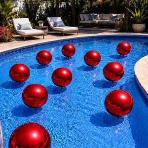 May include: A collection of ten smooth, reflective red spheres floating on the surface of a blue swimming pool. Each sphere has a glossy finish that catches the light, creating a vibrant contrast against the clear water of the pool.