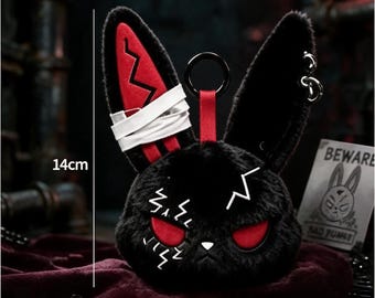 May include: A black plush rabbit head keychain measuring 14 cm in height. It features red eyes, white lightning bolt embroidery, a white bandage wrap on one ear, and a red strap with a black ring. A small card with the text BEWARE is visible.