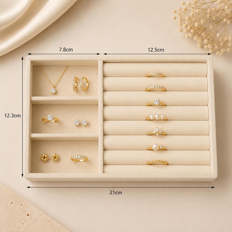 May include: A beige velvet jewelry organizer tray measuring 21 cm by 12.3 cm, featuring a left section with three compartments and a right section with seven ring slots. It holds gold necklaces, earrings, and rings with various stone settings.