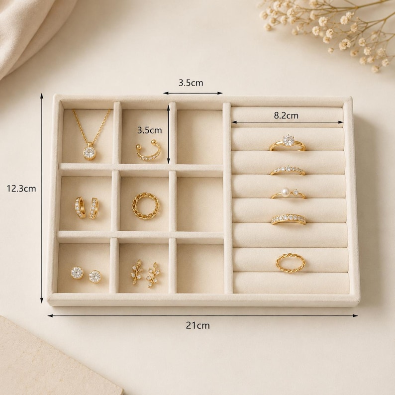 May include: A beige velvet jewelry organizer tray measuring 12.3 cm by 21 cm, featuring multiple compartments and ring slots. It contains gold-toned jewelry including a necklace, earrings, a cuff, and five rings with various stone settings.
