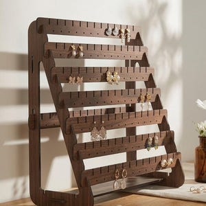 May include: A dark brown wooden earring display stand with multiple horizontal rows of holes for hanging earrings. The stand is angled and holds various styles of earrings, including studs and dangling designs. The stand is on a light-colored surface.