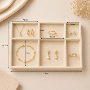 May include: A beige velvet jewelry organizer tray measuring 21 cm by 12.3 cm, containing gold-toned jewelry including a necklace, a bracelet with white beads, two rings, and four pairs of earrings. The tray features internal dividers with labeled dimensions.