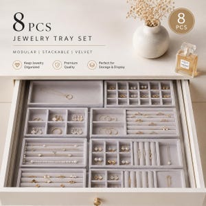 May include: An 8-piece modular and stackable gray velvet jewelry tray set arranged inside a drawer. The set includes various compartments for rings, necklaces, and earrings. Text on the image reads 8 PCS JEWELRY TRAY SET, MODULAR, STACKABLE, VELVET.