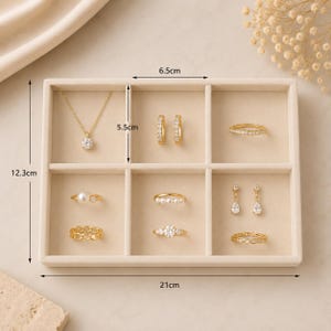 May include: A beige jewelry organizer tray with six compartments containing gold-toned jewelry, including a necklace, hoop earrings, drop earrings, and various rings. The tray measures 21 cm by 12.3 cm, with individual sections measuring 6.5 cm by 5.5 cm.