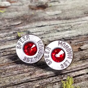 May include: A pair of silver bullet earrings with red rhinestones. The bullets are engraved with "SPEEER MAGNUM 357".