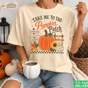 Può includere: Una t-shirt color avorio con una stampa grafica che riporta il testo "Take Me To The Pumpkin Patch". Il design include una grande zucca arancione, un girasole, foglie autunnali, un cartello in legno con la scritta "Farm Fresh" e "Daily Picked".