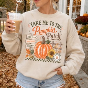 Può includere: Una felpa girocollo beige con una stampa grafica che recita Take Me To The Pumpkin Patch. Il design include una grande zucca arancione, un girasole, foglie autunnali, un cartello in legno e un distintivo con la scritta Good Times & Cozy Vibes.