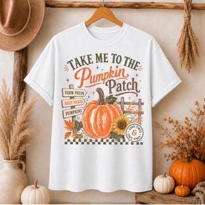 Può includere: Una t-shirt bianca con una stampa grafica di una grande zucca arancione, un girasole e cartelli in legno con le scritte Farm Fresh, Daily Picked e Pumpkins. È incluso il testo Take Me To The Pumpkin Patch e Good Times & Cozy Vibes.