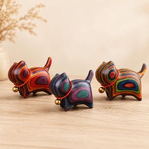 May include: Three small cat figurines crafted from multi-colored laminated wood. Each cat features a smooth, polished finish with swirling patterns of red, purple, blue, and green. A thin red cord with a small gold-toned metal bell hangs around each neck.