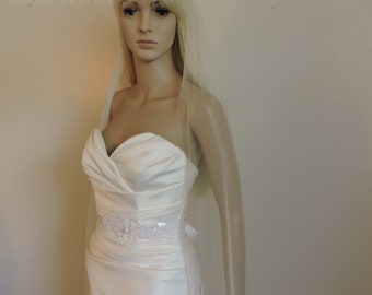 Può includere: Un abito da sposa bianco senza spalline con una cintura di perline e un velo di tulle avorio. L'abito ha un corpetto aderente e una gonna fluida.